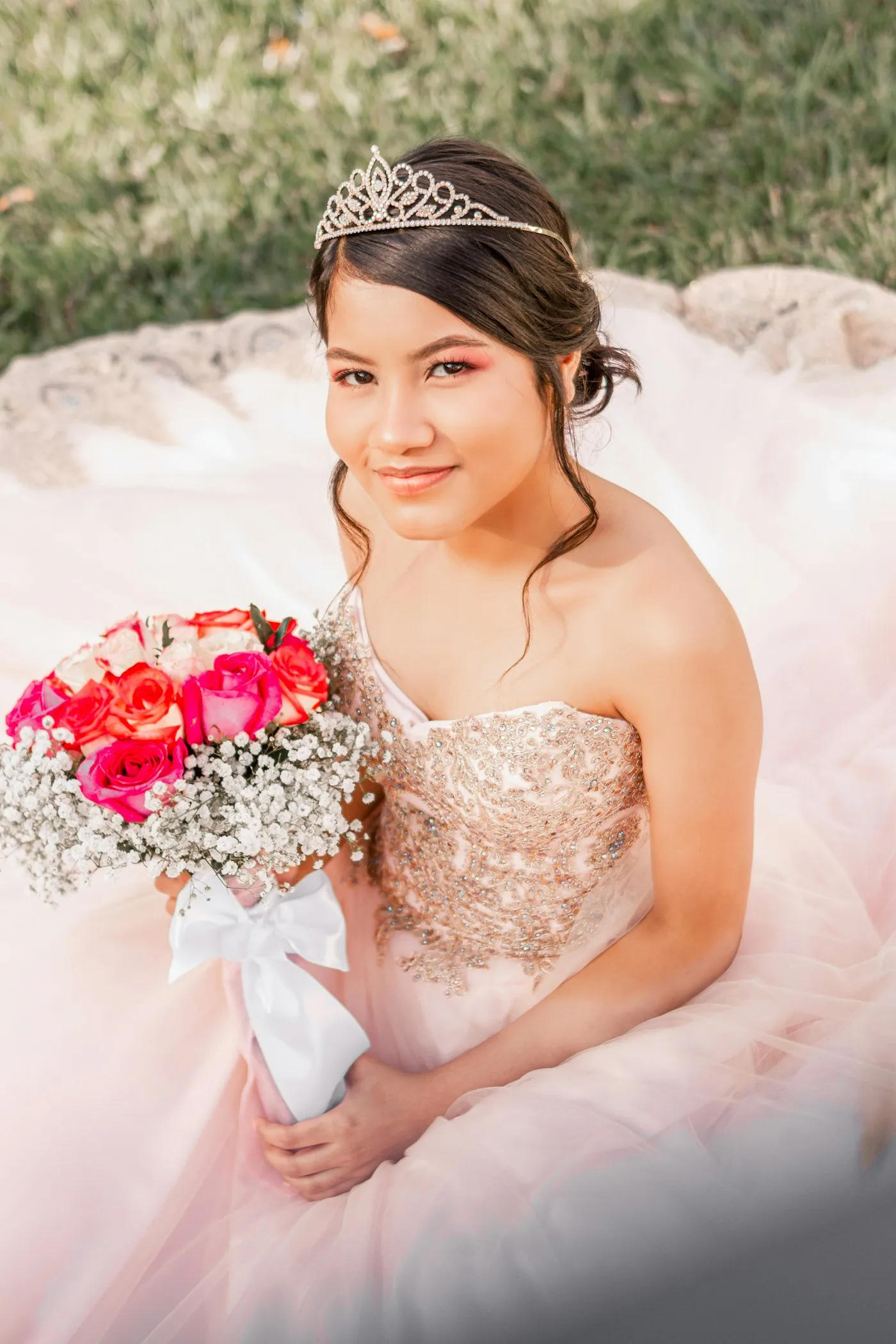 Quinceañera sonriendo con corona y ramo de rosas